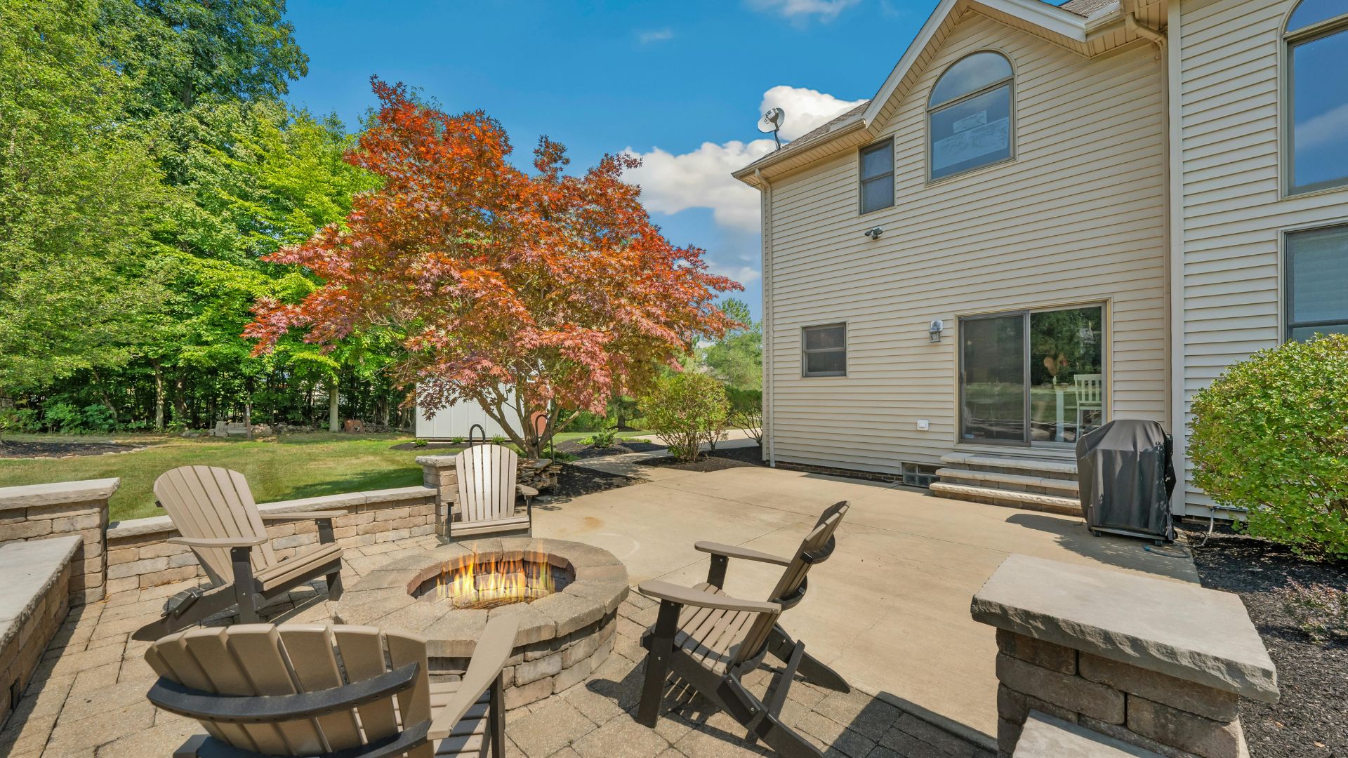 Outdoor patio with fire pit, Adirondack chairs, and colorful maple tree